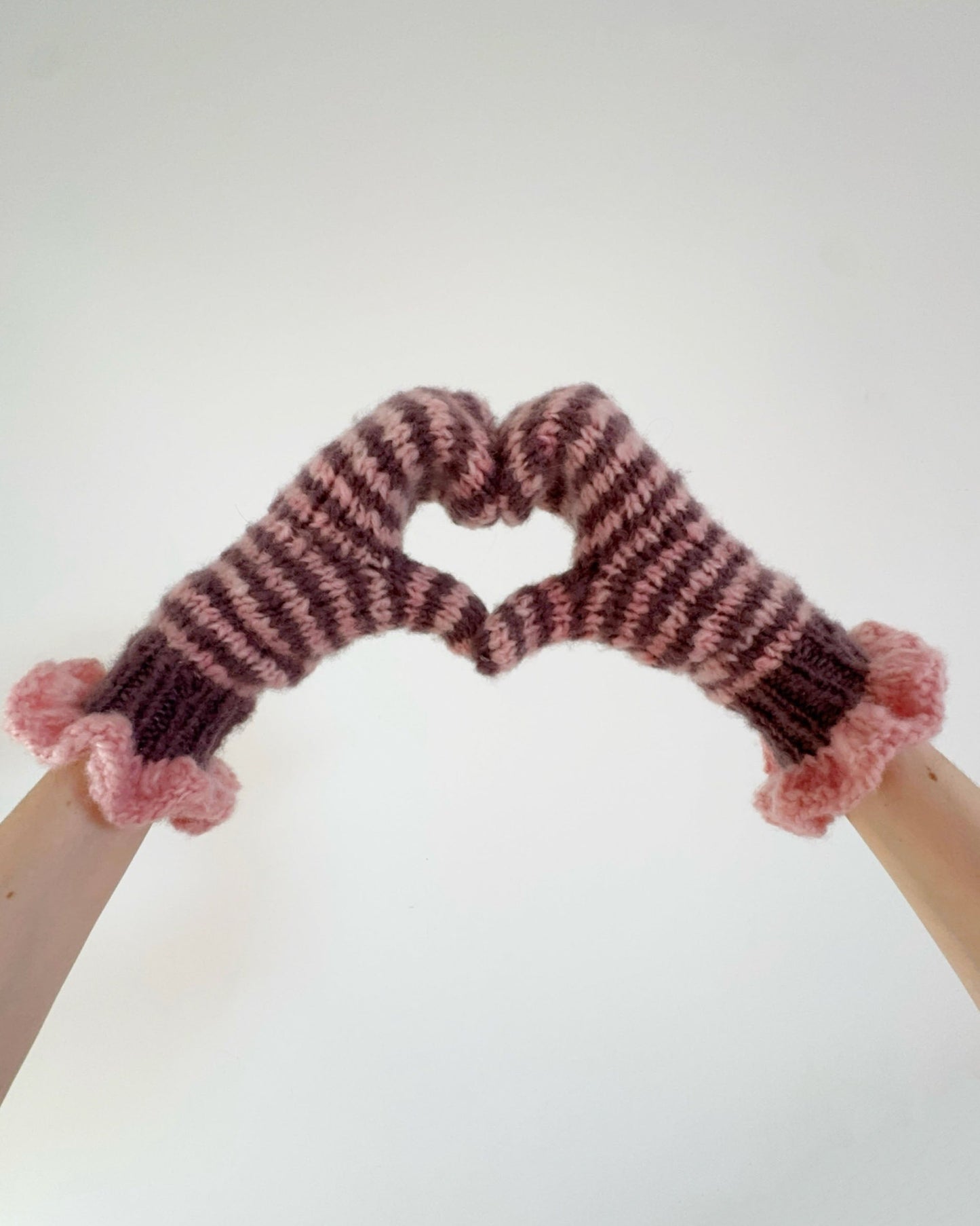 Pair of pink and chocolate striped mittens with frill cuffs on a white background